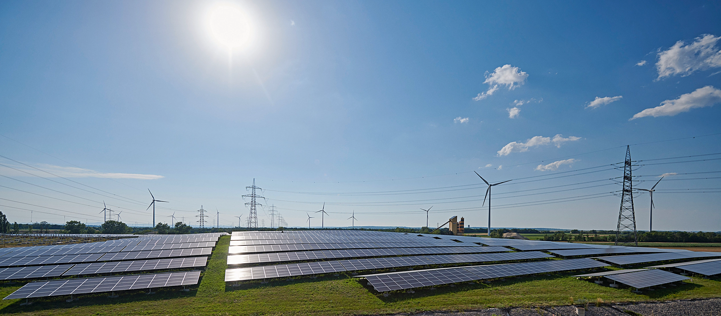 Wir blicken auf einige Windräder, Strommasten und Photovoltaik-Panele bei strahlendem Sonnenschein.